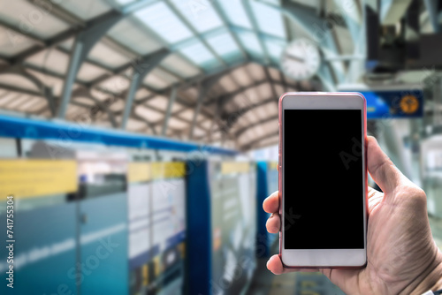 Close-up of a hand holding a blank-screen smartphone with a blurred train station background, suggesting travel and technology.. photo