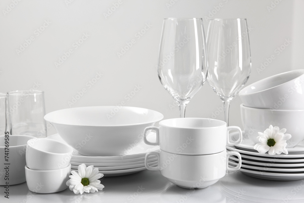 Set of many clean dishware, flowers and glasses on light table Set of many clean dishware, flowers and glasses on light table