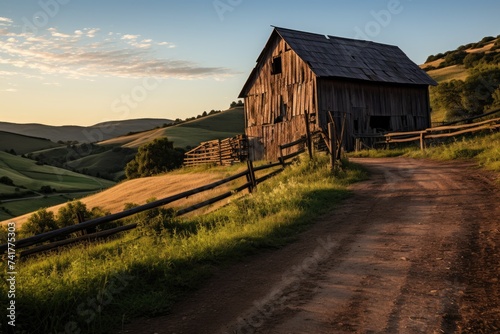 The warm evening sun bathes an old wooden granary and fence in golden light, with rolling hills stretching into the distance