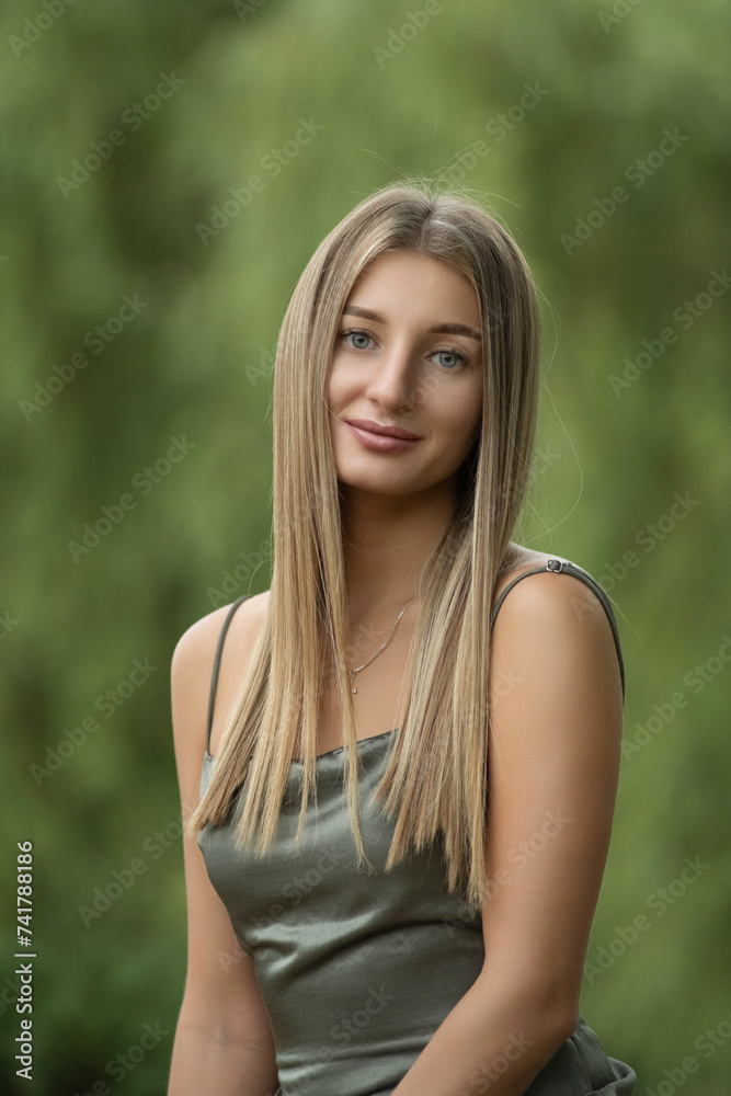 Portrait of a young beautiful blonde girl in a green dress in a city park. Portrait of a young beautiful blonde girl in a green dress in a city park.