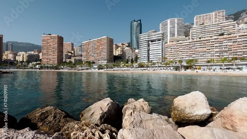 The famous beach Larvotto of principality of Monaco in sunny day, sun umbrellas, palm trees, azure water, large stones, residential complex photo