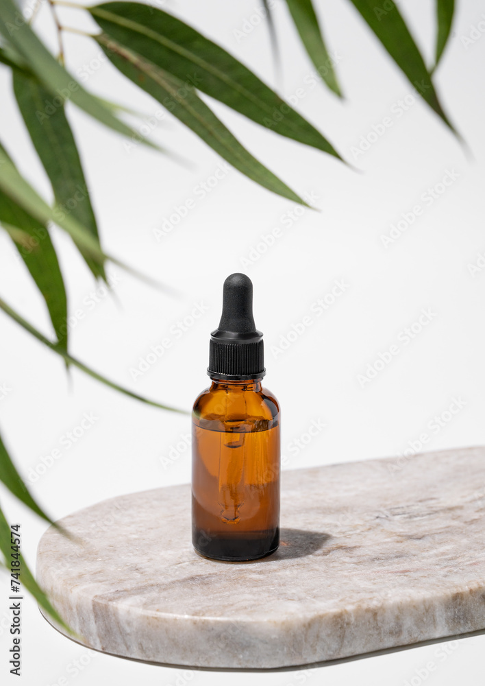 Face and body serum in bottle on a marble board on a white background with green leaves and shadow. Face and body serum in bottle on a marble board on a white background with green leaves and shadow.