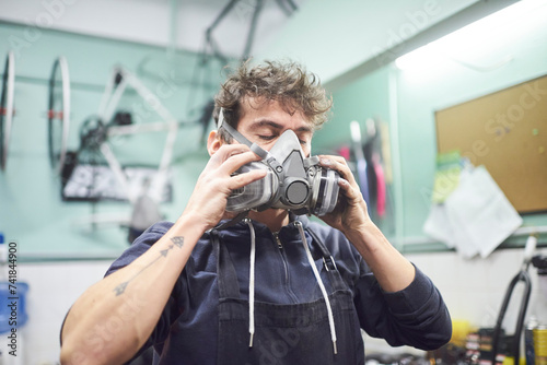 Portrait of a latin young worker removing a respiratory protection mask, as he finishes a spray painting job in his workshop. Health protection in industrial work. Real people working. photo