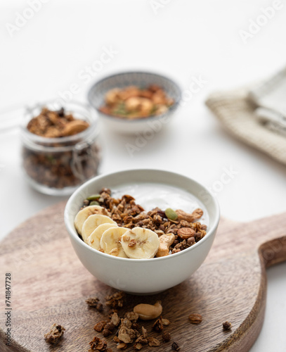 Baked granola with yogurt and banana on a cutting board on a white table.