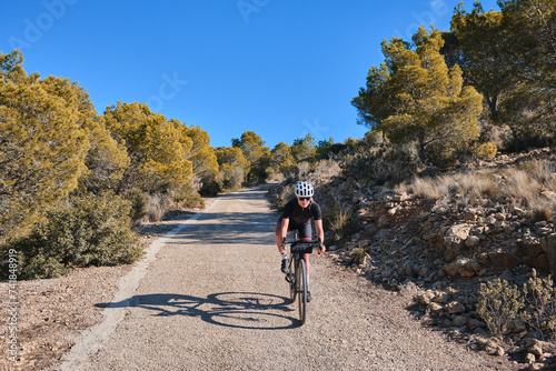 Woman cyclist riding a gravel bike with a view of the Spanish mountains. Fit athlete wearing sportswear and helmet.Sports motivation image. Good road for cycling. Alicante, Spain.