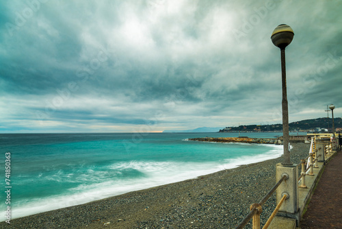 The landscape of Varazze, Liguria, Italy in winter, during a rainy day, with dramatic clouded sky. Blurred blue waters of mediterranean sea on the left. Dark clouds on top. photo