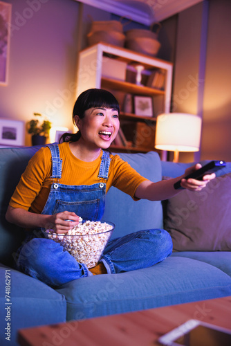 Woman turning on TV using remote control relaxing at home late at night photo