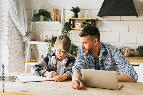 family dad young man with phone and son teenage cute boy with tablet and headphones doing homework sit at table in cosy apartment, quality time with your family, gadget addicted, education