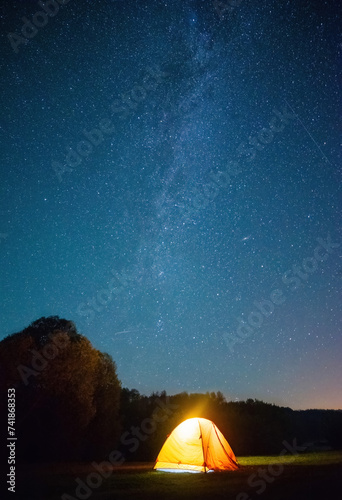 night shot capturing a yellow tent lit up from within, and the awe-inspiring Milky Way and stars in the dark night sky.