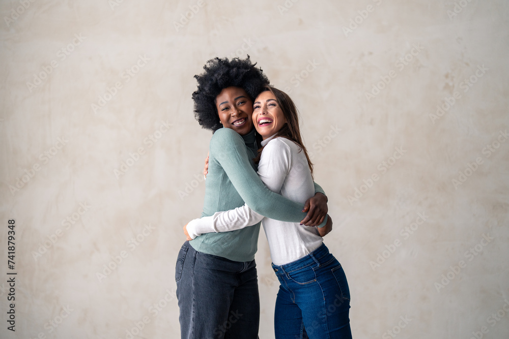 Two smiling interracial women embracing while standing in a studio.