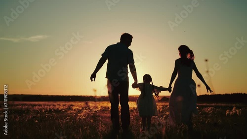 Small girl happily runs hand in hand with parents on field to release energy after day at kindergarten. Small girl loves to run across field at sunset having fun with papa and momma at sunset photo