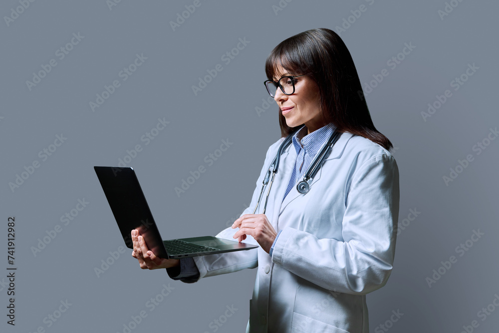 Profile portrait of female doctor using laptop on gray background Profile portrait of female doctor using laptop on gray background