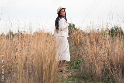 Mujer con sombrero y vestido blanco en un prado rodeada de naturaleza