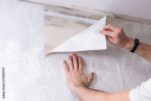 A man is gluing non-woven wallpaper on the wall. Room renovation