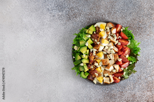 Classic American Cobb salad with tomatoes, bacon, chicken, eggs, avocado and blue cheese on a gray background. Top view. Copy space. photo