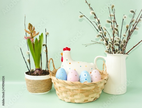 Easter composition, decorative chicken with Easter eggs in a wicker basket on the table and spring hyacinth flowers, willow twigs, a symbol of Easter.  Front view, space for copying text.