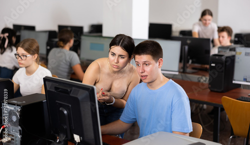 Focused female teenager helping to the male classmate while he is learning computer science in the class.