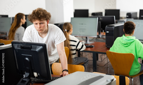 Teenage boy sitting at table and using computer during lesson.