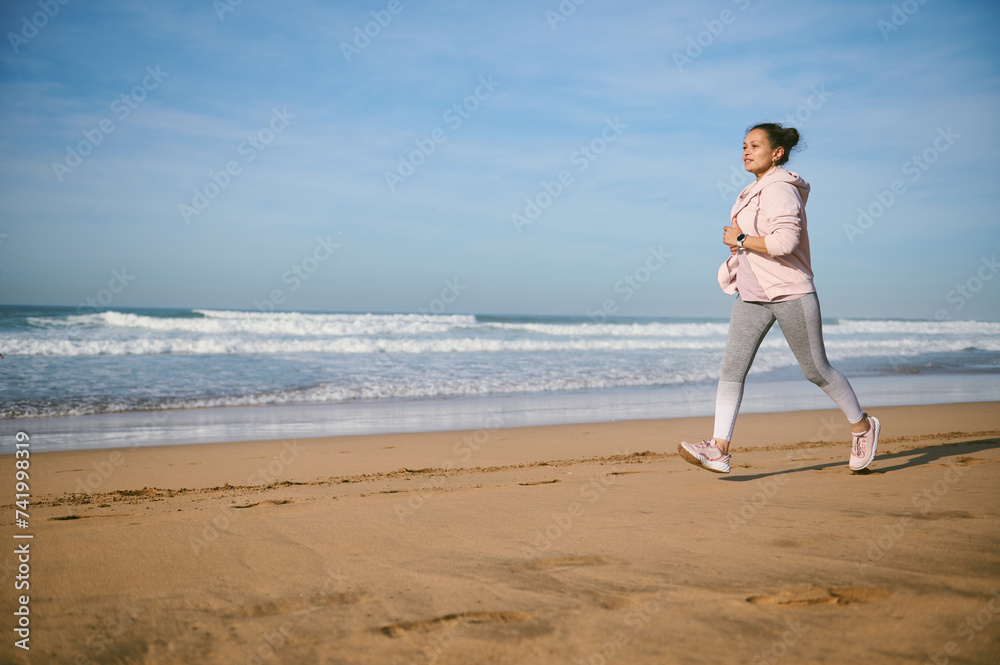 Middle aged Latin American woman jogging on the beach. People and outdoor workout. Active healthy lifestyle concept Middle aged Latin American woman jogging on the beach. People and outdoor workout. Active healthy lifestyle concept