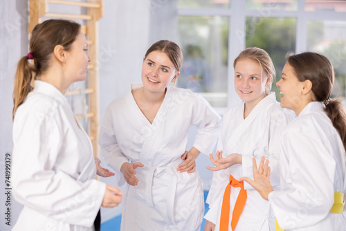 Cheerful happy teenage girls wearing white kimonos chatting and laughing animatedly during break in martial arts training..