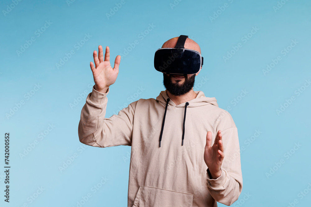 Young gamer enjoying metaverse with virtual reality headset. Man wearing vr helmet exploring entertainment activity in cyberspace while standing and making gesture with arms