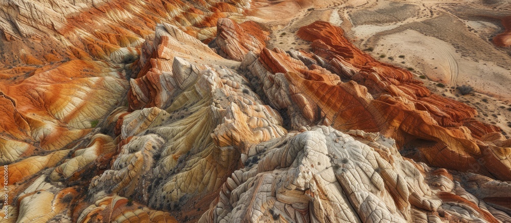 The aerial view shows a mountain range with vibrant colors, including red rocks and beige sandstones. The landscape is filled with various hues that create a striking contrast. The aerial view shows a mountain range with vibrant colors, including red rocks and beige sandstones. The landscape is filled with various hues that create a striking contrast.