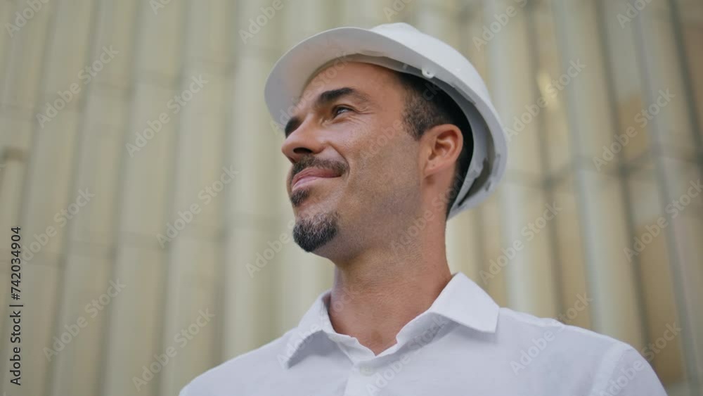 Portrait latin builder smiling camera at architecture background. Man n hardhat