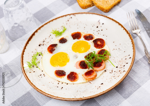 Fried Vienna sausages slices with fried eggs served with dill leaves and bread toasts .