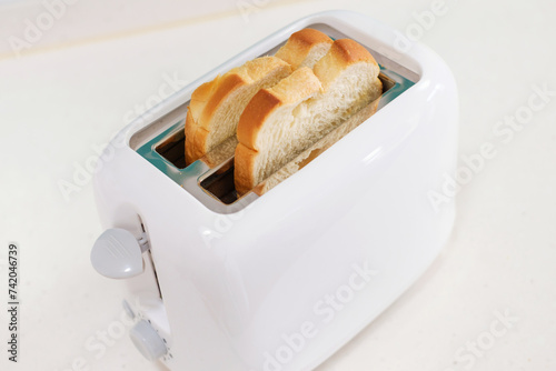 Pieces of bread in a toaster on white background, side view.