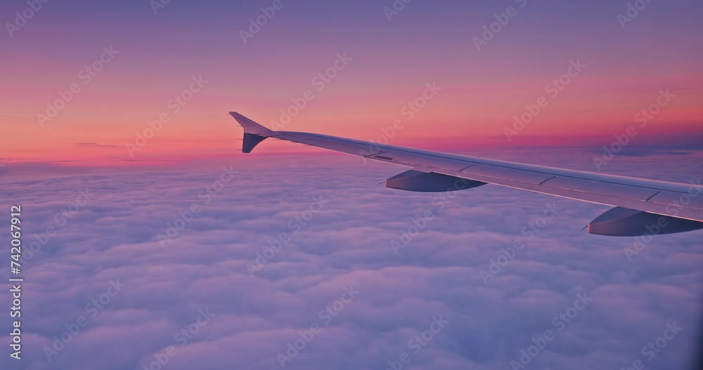 Airplane flying over color sky clouds during scenic sunset or sunrise cloudscape, view from plane window of wing turbines and horizon 4k video