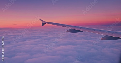 Airplane flying over color sky clouds during scenic sunset or sunrise cloudscape, view from plane window of wing turbines and horizon 4k video
