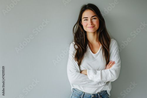 Confident Young Woman in Classic White Tee and Jeans Posing with Arms Crossed Against a Plain Grey Wall