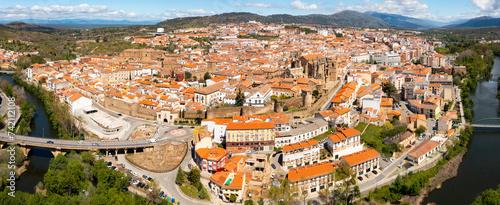 View from drone of residential area of Plasencia city with brownish tiled roofs of houses and ancient gothic roman catholic cathedral on green bank of meandering Jerte river in spring, Caceres, Spain photo