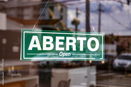 Bilingual sign with the words Aberto and Open in Portuguese and English on the glass door of a store in Brazil photo