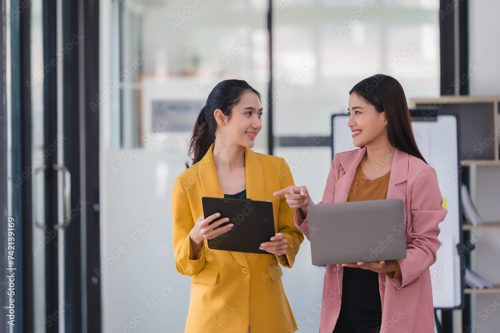 Two beautiful Asian businesswoman golding digital tablet and laptop, standing in the office room. Two beautiful Asian businesswoman golding digital tablet and laptop, standing in the office room.