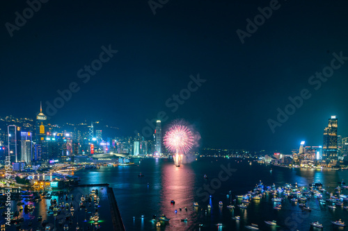Fireworks burst brightly against the night sky above a city skyline  reflecting in the calm water below