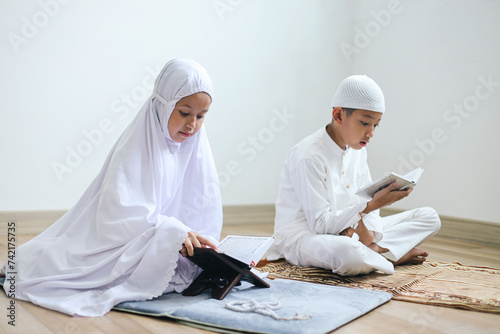 фотографія Asian muslim little boy and girl sitting on floor and reading Al Quran together