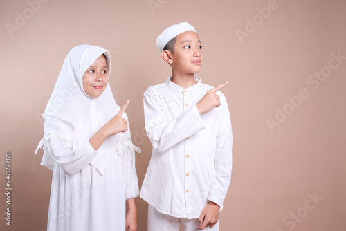 Young Asian moslem boy and girl in traditional muslim clothes pointing aside to the copy space for text and ads