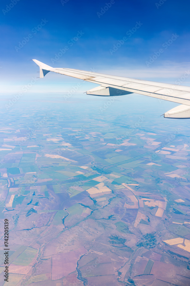 Obraz premium Aerial view from airplane window above green ground. View from the airplane window with beautiful clouds at sunrise