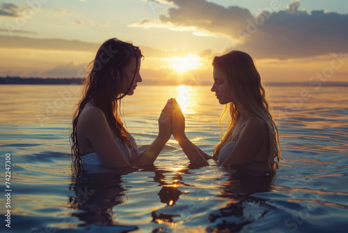 Baptism. Portrait of two young woman praying in the water at sunset photo