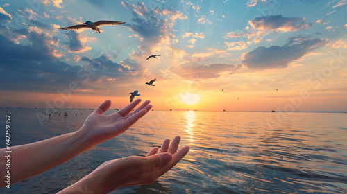 hand holding a sun. Hands open palm up worship with birds flying over calm water sunset background. Concept of praying for blessing from God © FH Multimedia