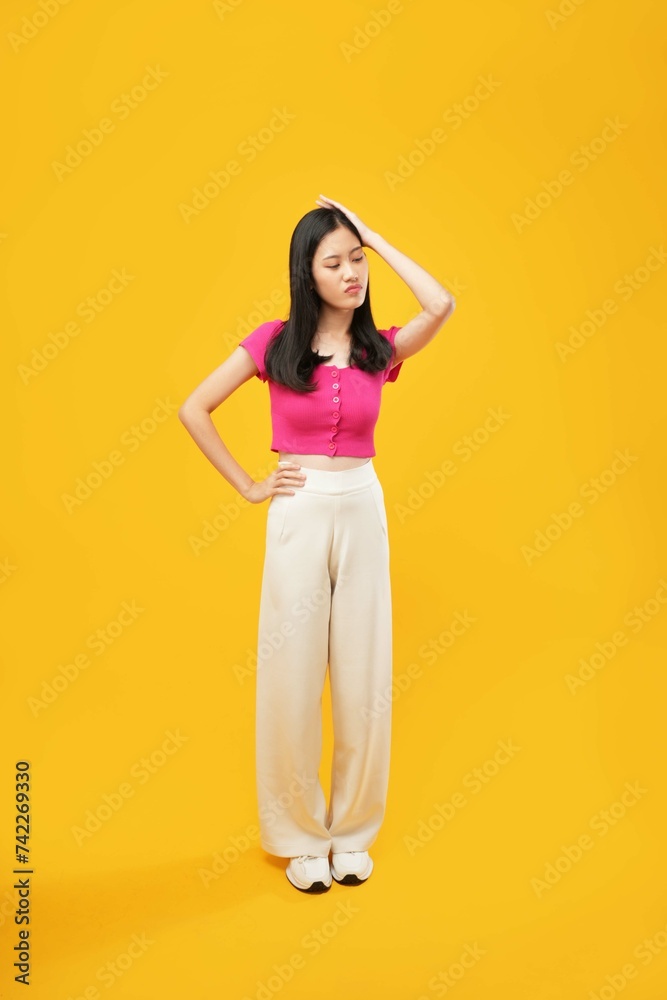 Full-length portrait of amazed excited young Asian woman in a pink casual t-shirt thinking something isolated on Yellow color wall background studio