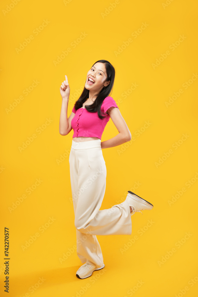 Full-length portrait of amazed excited young Asian woman 20s in a pink casual t-shirt pointing index fingers aside up on mock-up copy space isolated on Yellow color wall background studio Full-length portrait of amazed excited young Asian woman 20s in a pink casual t-shirt pointing index fingers aside up on mock-up copy space isolated on Yellow color wall background studio