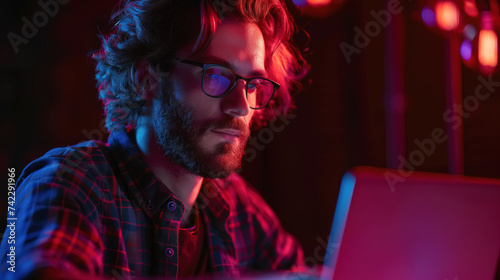 Man with glasses is focused on his laptop screen, working on an online course or training. He appears interested and attentive to the content displayed on the computer