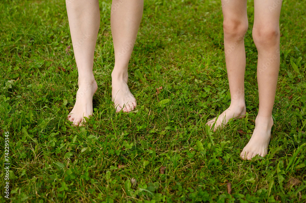 Woman and a child walk together barefoot on the grass on a lawn in a city park. The concept of a healthy lifestyle, freedom and outdoor recreation.