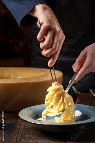 The chef prepares tagliatelle pasta with sun-dried tomatoes and basil in a large head of parmesan cheese. Alfredo Italian pasta photo