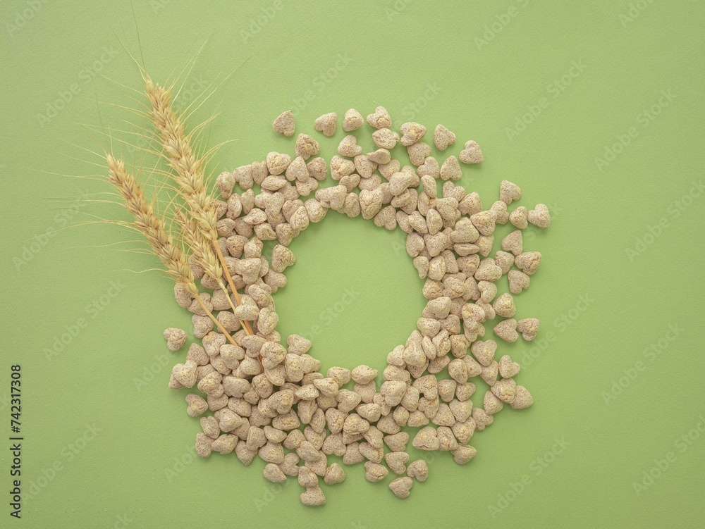 Obraz premium Extruded heart-shaped bran is poured onto a green background forming a circular void space for the text. Spikelets of wheat. The concept of proper snacking, proper nutrition and weight loss