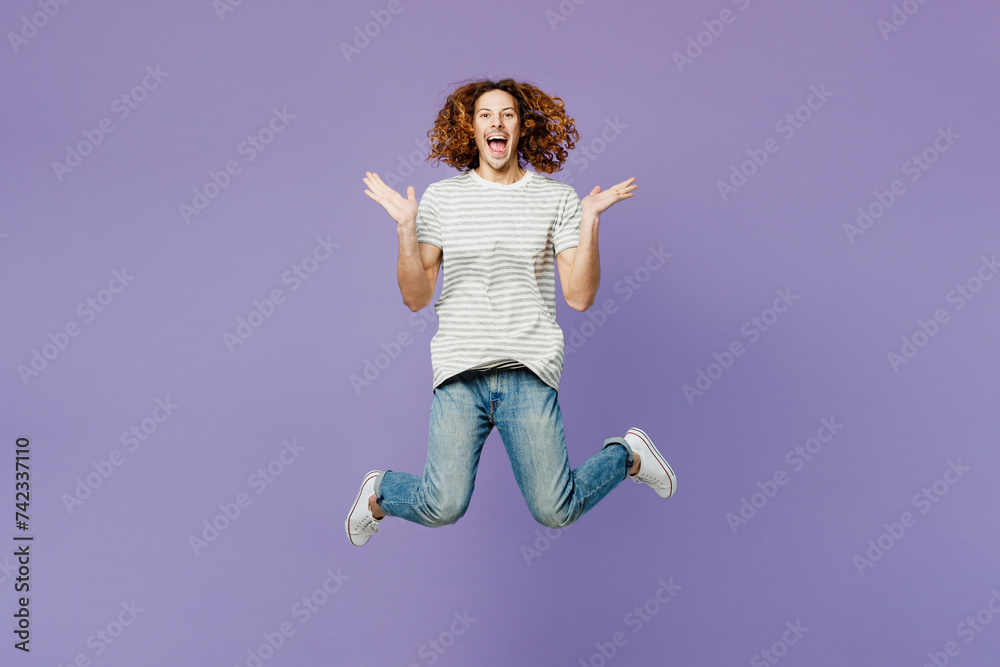 Full body shocked surprised young man wears grey striped t-shirt casual clothes jump high spread hands look camera isolated on plain pastel light purple background studio portrait. Lifestyle concept.