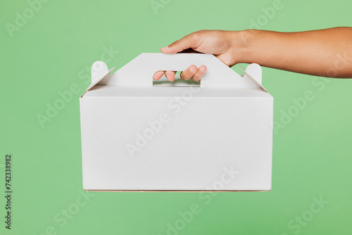 Close up cropped delivery guy male employee courier hold in hand cake dessert in blank cardboard box isolated on pastel plain green background studio. Service concept. Copy space advertising mock up. photo