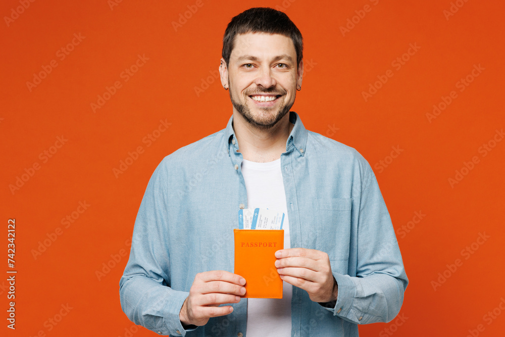 Traveler man wear blue shirt casual clothes hold passport ticket isolated on plain red orange background studio. Tourist travel abroad in free spare time rest getaway. Air flight trip journey concept. Traveler man wear blue shirt casual clothes hold passport ticket isolated on plain red orange background studio. Tourist travel abroad in free spare time rest getaway. Air flight trip journey concept.